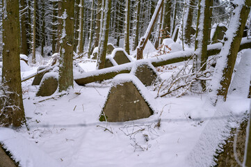 Medium shot of anti tank dragon's teeth covered by snow in a forest 