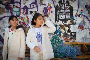Two young asian girls stadning in front of street grafitti in New York City