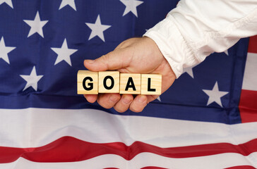 Against the background of the USA flag, a man's hand with cubes with the text - GOAL