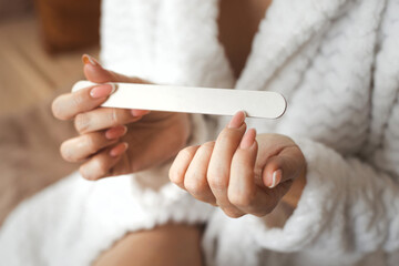 Closeup photo of young womans hand makes herself a manicure, files her nails with a nail file....