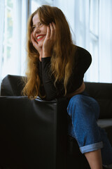 Brunette girl in the blue jeans is sittieng  on a black sofa and smileing 