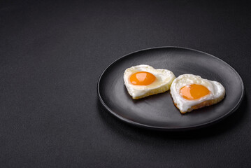 Two heart-shaped fried eggs on a black ceramic plate on a dark concrete background