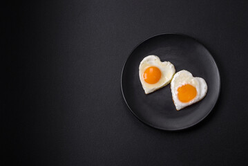 Two heart-shaped fried eggs on a black ceramic plate on a dark concrete background