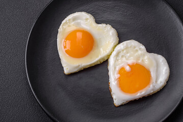 Two heart-shaped fried eggs on a black ceramic plate on a dark concrete background