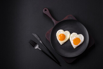 Two heart-shaped fried eggs on a black ceramic plate on a dark concrete background