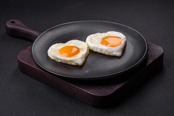 Two heart-shaped fried eggs on a black ceramic plate on a dark concrete background