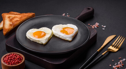Two heart-shaped fried eggs on a black ceramic plate on a dark concrete background