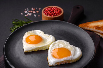 Two heart-shaped fried eggs on a black ceramic plate on a dark concrete background