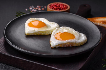Two heart-shaped fried eggs on a black ceramic plate on a dark concrete background