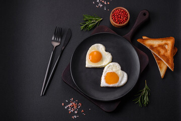 Two heart-shaped fried eggs on a black ceramic plate on a dark concrete background