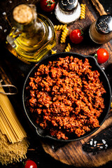 Bolognese sauce on a cutting board with cherry tomatoes and dry pasta. 