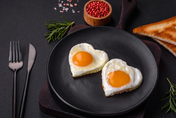 Two heart-shaped fried eggs on a black ceramic plate on a dark concrete background
