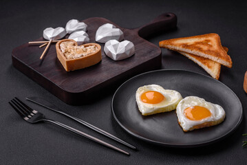 Two heart-shaped fried eggs on a black ceramic plate on a dark concrete background