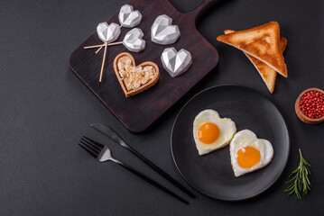 Two heart-shaped fried eggs on a black ceramic plate on a dark concrete background