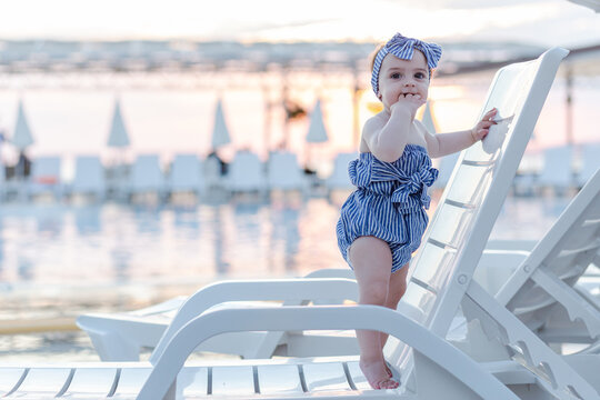 Cute little toddler baby girl standing on sunbed. Summer season resort concept. Space for copy.