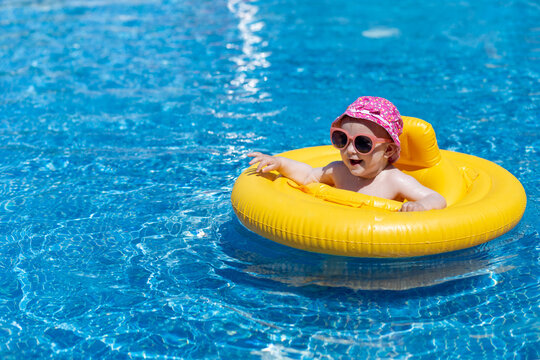 Sweet toddler baby girl in pool float ring enjoying summer day in swimming pool. Space for copy.