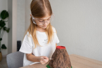 Child schoolgirl make volcano model for chemical experience. Home education.