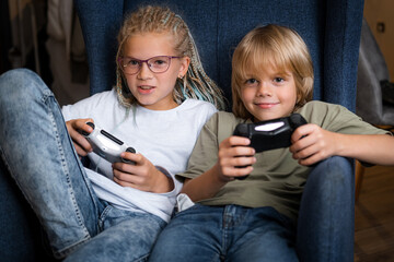 boy and girl playing video game console using joystick or controller while sitting at home, Two children small caucasian brother and sister happy children siblings, real people family leisure concept. © FOTO_STOCKER