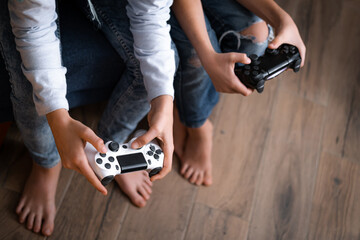 kids hands with joysticks, two children siblings playing video game console while sitting at home,...