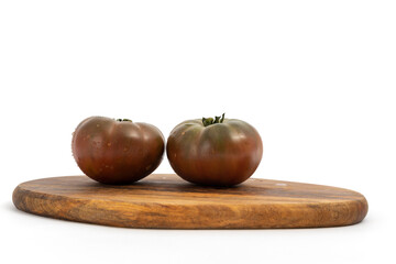 Black tomatoes on wooden chopping board on white background isolated