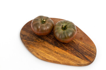 Two black tomatoes on wooden chopping board on white background isolated