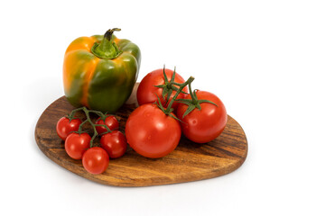 Green pepper and cherry tomatoes on wooden chopping board on white background isolated