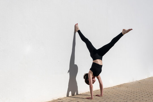 Woman doing a handstand against a white wall in the sun