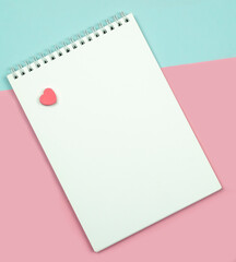 Blank notepad top view on blue and pink background .Small red heart as a symbol of love,valentine's day. Copy space 