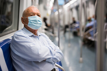 Fototapeta na wymiar Old European man in face mask sitting inside subway train and waiting for next stop.