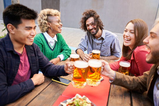 Happy people having fun drinking beer on terrace at dinner party. Young friends eating food at restaurant together. High quality photo