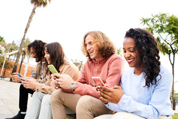 Friends having fun sharing in social media. Smiling mixed race group of friends sitting together on bench using mobile phone in the park. High quality photo