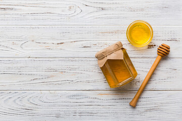 Glass jar of honey with wooden drizzler on colored background. Honey pot and dipper high above. Top view copy space