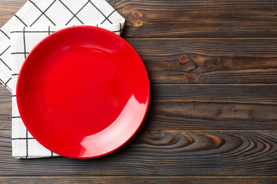 Top View On Colored Background Empty Round Red Plate On Tablecloth For Food. Empty Dish On Napkin With Space For Your Design