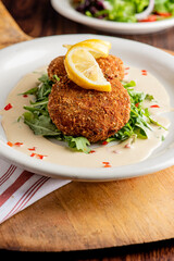Crab cake. Crab cake served with spicy rémoulade sauce on top of a mixed green salad. Jumbo crab meat mixed with garlic, onions, spices and fried in butter. Classic American restaurant appetizer.