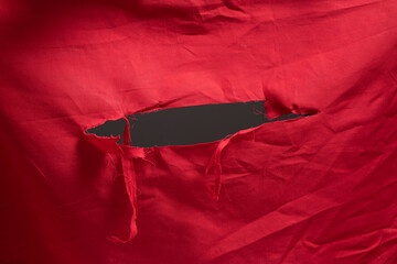 red fabric with big hole and shredded threads, ripped open hole at center of a red flag
