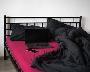 Laptop with black blank screen display and smartphone on bed with viva magenta color bedsheet and black blanket and pillows. Freelancer, blogger, outsourcing business.  Copy space, mockup, template