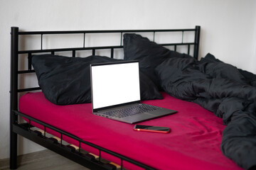 Laptop with black blank screen display and smartphone on bed with viva magenta color bedsheet and black blanket and pillows. Freelancer, blogger, outsourcing business.  Copy space, mockup, template