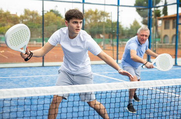 Fototapeta premium Young man in sportswear playing padel tennis match during training on court