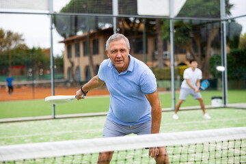 Obraz premium Emotional mature man playing paddle tennis couple match at outdoors court. Health and active lifestyle concept