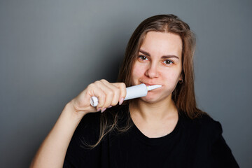 Obraz premium Portrait of a smiling young woman without makeup in a black t-shirt brushing her teeth, mature woman, natural beauty concept. Morning brush for teeth, dental ultrasonic brush.
