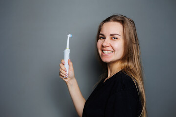 Obraz premium Portrait of a smiling young woman without makeup in a black t-shirt brushing her teeth, mature woman, natural beauty concept. Morning brush for teeth, dental ultrasonic brush.
