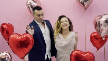 Beautiful Valentine's Day couple in red and pink balloons celebrating February 14, love. Woman in evening dress and guy in suit dancing laughing and having fun, party.