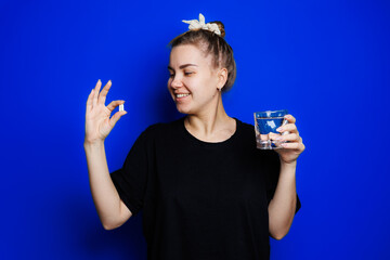 Smiling young woman without makeup in black t-shirt drinking vitamins for health, mature woman, natural beauty concept. Morning glass of water, immune care, vitamin complex for women. Selective focus