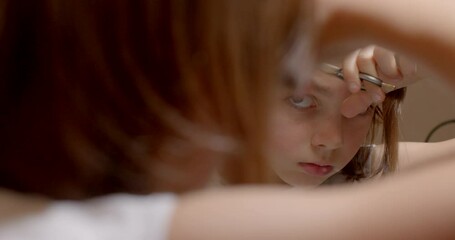 A teenage boy cuts his hair with scissors, shooting through his hand in bokeh. Do your own hair at home. Use a mirror for manual haircuts.