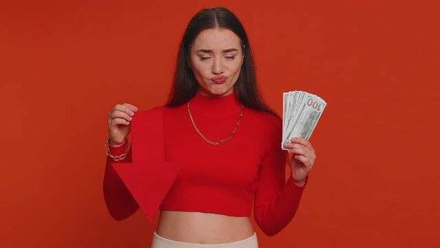 Upset pretty woman showing red arrow pointing down, concept of downgrade, unsuccessful business, fall of stock market money dollar exchange rate bankruptcy fail. Young adult girl on red background