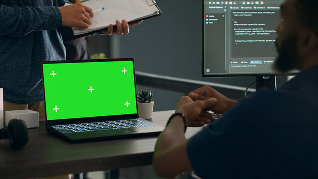 Database admins analyzing source code and greenscreen display on computer to develop software algorithm in busy space. Cloud programers working with chromakey template isolated copyspace.