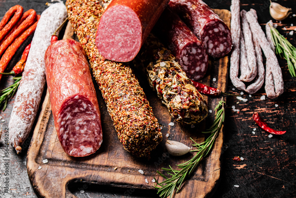 Poster Different types of salami sausage on a cutting board with rosemary. 