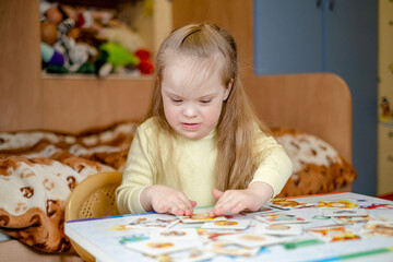 A little girl with Down Syndrome is engaged in educational activities with educational cards.
