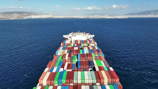 Aerial drone top down tracking video of huge Container cargo Ship carrying load in truck-size colourful containers cruising deep blue Aegean sea, Greece