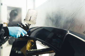 Close-up of person wearing blue gloves painting part of car black using airbrush. Car paintwork....